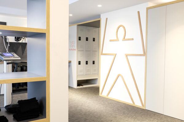 Studio ergonomique blanc et bois. Couloir donnant sur le mur avec le logo en plainte en bois et sur les casiers.